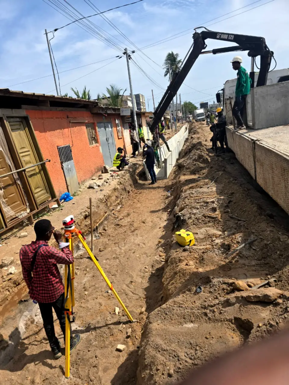 Topographe d’Ets Gana Ousmane au théodolite devant un ouvrage en béton armé et une grue de chantier